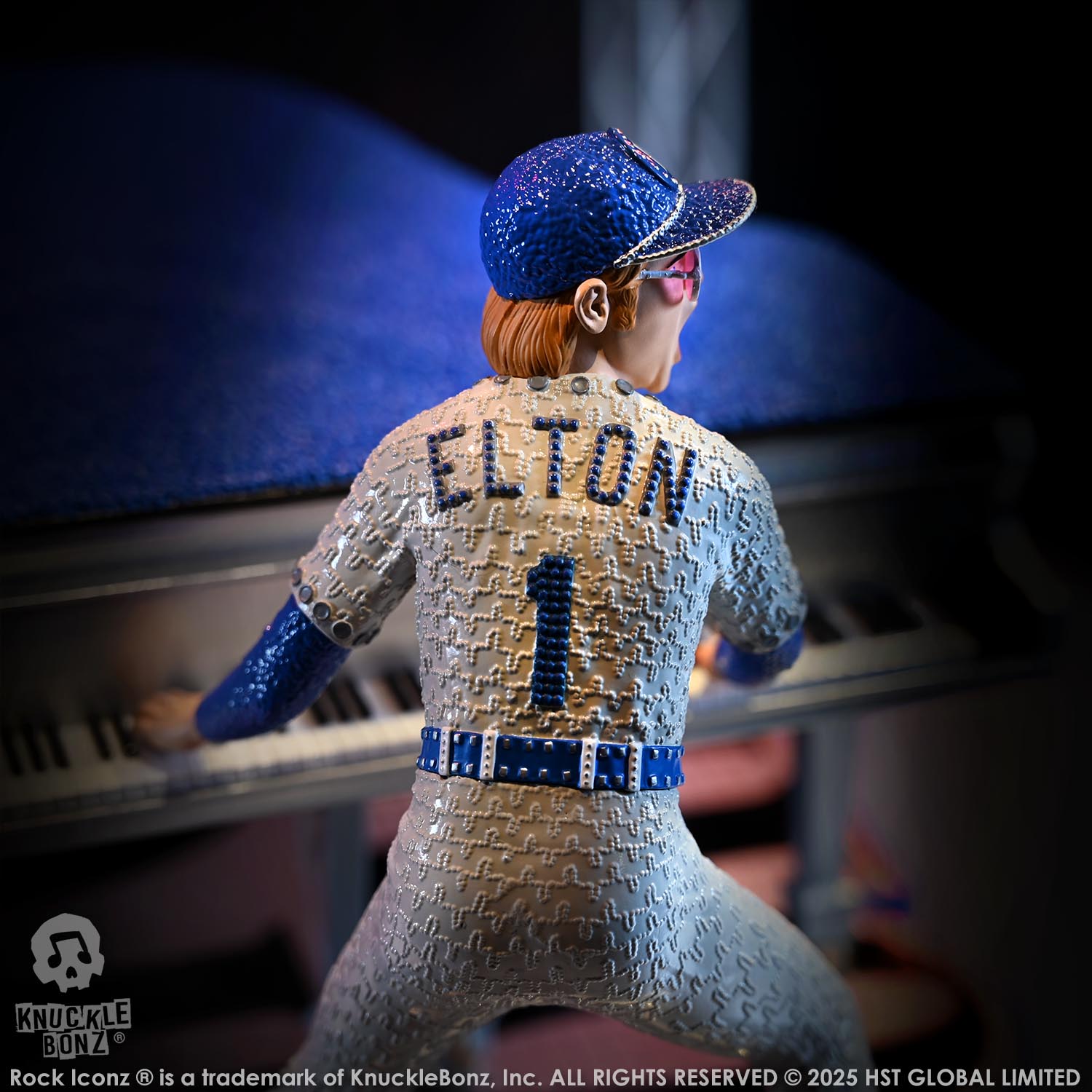Statue of Elton John with a grand piano in in a blue and white uniform with 'Elton' and number '1' on the back, wearing a blue cap.